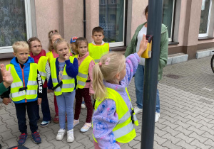 Dziewczynka włącza przycisk przy sygnalizatorze świetlnym w celu przejścia na drugą stronę.