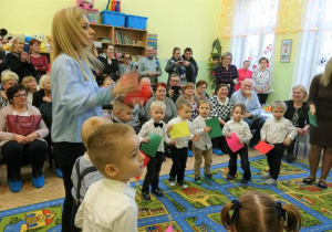 Dzieci stoją w kółeczku i trzymają w rączkach kolorowe kartony.