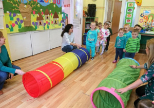 Dzieci ustawione w pociąg przechodzą kolejno przez tekstylne tunele.