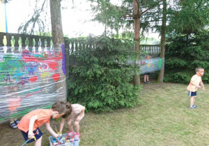 2 dzieci maluje na folii zawieszonej między drzewami.