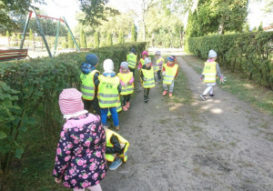Dzieci zbierają papierki w ogrodzie przedszkolnym.