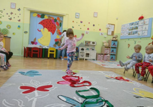 Dziecko idzie po rozłożonych na dywanie kolorowych szarfach.