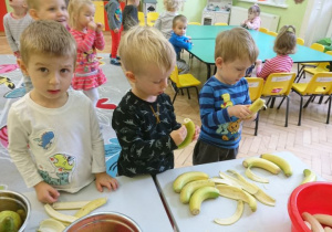 3 chłopców obiera banany ze skórki.
