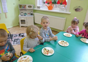 Dzieci siedzą wokół stołu, przed sobą mają talerzyki z kawałkami owoców.