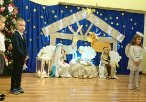 Dzieci na tle świątecznej dekoracji prezentują Jasełka.