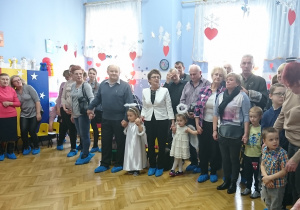 Przedszkolaki stoją razem z dziadkami i babciami.