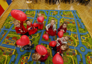 Przedszkolaki trzymają czerwone baloniki w kształcie serduszek.