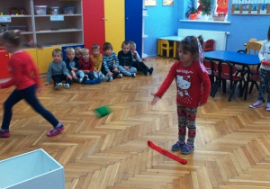 Dziewczynka rzuca woreczkiem do niebieskiego pudełka stojącego na środku sali.