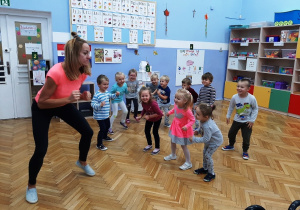 Dzieci w pozycji stojącej naśladują ćwiczenia pokazywane przez nauczycielkę.