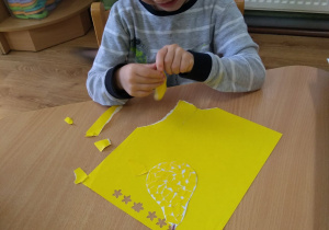 Chłopiec wykleja kontur gruszki skrawkami żółtego papieru.