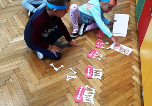 3 dzieci na podłodze przyporządkowuje papierowe kości do rysunków miseczek z określoną liczbą kropek
