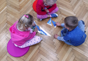 3 dzieci układa obrazek z krajobrazem z pociętych elementów.