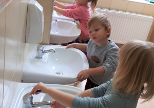 4 dzieci stoi przy umywalkach i odkręca wodę.