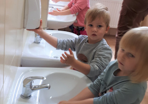3 dzieci myje rączki przy umywalce, czwarte nabiera z podajnika mydło w płynie.