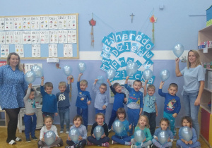 Grupa dzieci z niebieskimi balonami na tle dekoracji.