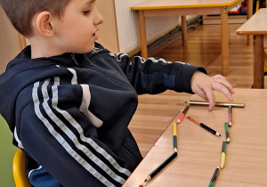 Chłopczyk układa różne wzory z kredek na blacie stolika.