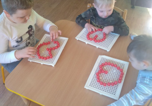 3 chłopców przy stoliku układa czerwone serduszka z pionków układanki.