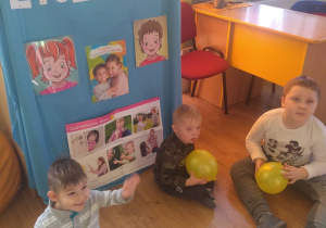 3 chłopców siedzi na tle dekoracji z żółtymi balonami w rączkach.