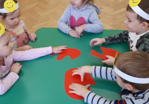 5 dzieci przy stoliku składa w całość czerwone serce wycięte z kartonu.