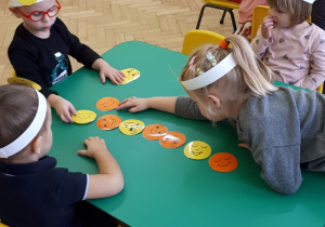 Dzieci przy stoliku układają kolorowe buźki według kodu.