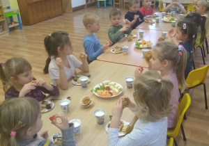 Dzieci jedzą słodki poczęstunek przy stole.