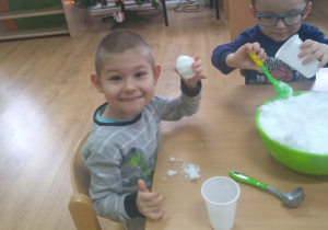 2 chłopców lepi kule ze śniegu przy stoliku.