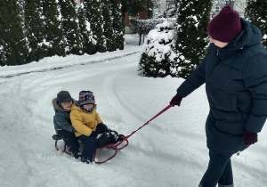 Nauczycielka ciągnie 2 dzieci na sankach.