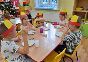 Dzieci siedzą przy stoliku i jedzą wafelki posmarowane miodem.