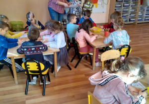 Dzieci siedzą przy stołach i rozwiązują łamigłówki w kartach pracy.