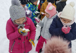 Grupa dzieci bawi się śniegiem w ogrodzie przedszkolnym.