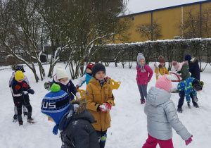 Grupa dzieci lepi śniegowe kule w ogrodzie przedszkolnym.