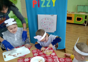 Trzech chłopców kroi produkty na pizzę.