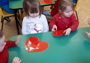 Dzieci przy stolikach składają w całość serduszka pocięte na części.