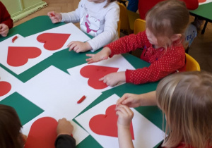 Przedszkolaki ozdabiają plasteliną czerwone serca.