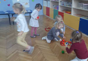 Dziewczynki układają kuleczki w rozłożonych na podłodze czerwonych szarfach.