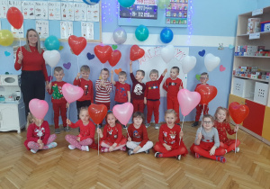 Grupa dzieci z balonami na tle walentynkowej dekoracji.