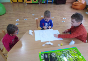Trzech chłopców przy stoliku wykonuje pracę plastyczną, wyklejają sylwetę niedźwiedzia watą.