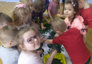 Grupa dzieci wykonuje pracę plastyczną "Dinozaury" farbami i folią bąbelkową.