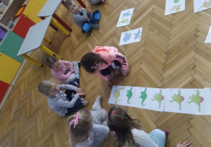 Dzieci układają domino obrazkowe z dinozaurami.