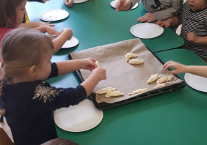 Przedszkolaki układają rogaliki na formie do pieczenia.