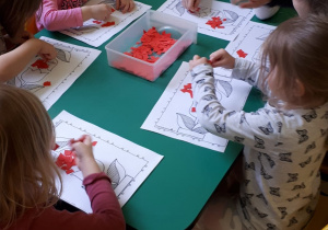 Dzieci przy stoliku wyklejają kwiatka kolorowym papierem.