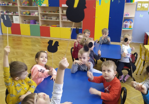 Grupa dzieci siedzi przy 2 stolikach z postaciami bajkowymi w rękach.