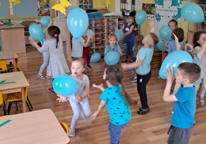 4 - 5 latki stoją w rozsypce i podrzucają błękitne balony.