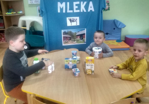 3 dzieci ogląda przy stoliku produkty mleczne.