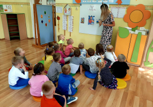 Dzieci siedzą na podłodze. Ciocia Basia pokazuje dzieciom obrazek przedstawiający chłopca, który leci na słoniu.