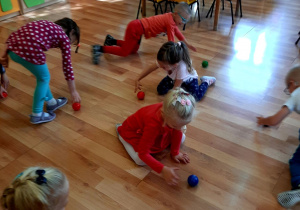 Dzieci turlają po podłodze kolorowe piłeczki