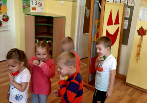 Dzieci trzymają pod brodą kolorowe piłeczki i próbują z nimi maszerować.