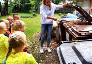 ciocia Basia pokazuje dzieciom, co należy wrzucać do kosza w kolorze brązowym.