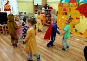 Dzieci tańczą w parach do piosenki "Malowała jesień". W tle widać kolorowe liście, litery, oraz dziewczynkę z parasolką wyciętą z papieru.