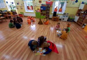 Dzieci siedzą na podłodze i układają pocięte w całość obrazki przedstawiające jesień.